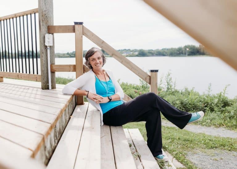 Steph Walker sitting on the steps of a wooden gazebo by the water
